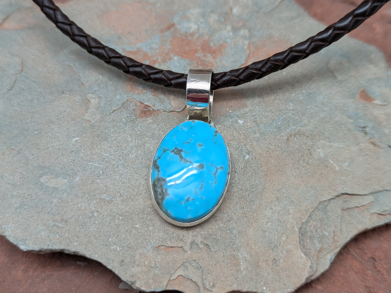 Turquoise and Sterling Silver Pendant Necklace. Brown braided leather necklace with lobster clasp. Color and matrix of the turquoise stone varies.